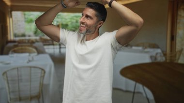 Çıplak kollarını gösteren ve restoran yemek alanında gülümseyen bir adam, mutluluğu kutluyor..