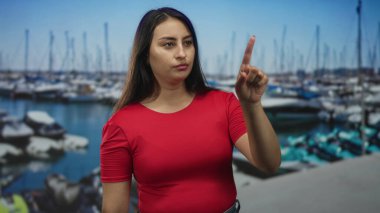 Stüdyo marinadaki kırmızı t-shirt ve kot pantolon giyen tekneleri işaret eden kadın, odaklanmış bakış ve görünür el hareketi; odaklanma niyeti.