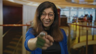 Kahverengi saçlı bir kadın sıcak bir gülümseme ve modern bir otel binasında uzanan elini gümüş bir kredi kartı uzatır; hoş geldiniz.