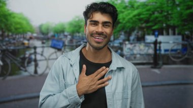 Adam kanalın yanında durur ve arkada bisikletlerle göğüs göğüse oturur, içten bir gülümsemeyle; minnettarlık.