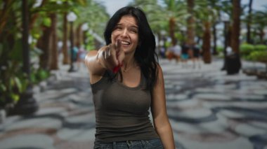 Palmiye ağaçlarının arasında elini uzatan İspanyol kadın gülerken ve ağzını eliyle kapatırken; neşe.