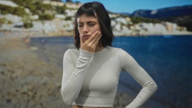 Kadın çeneye dokunur ve sahilde düşünceli bir duruş ve uzak bakışla işaret parmağını kaldırır..