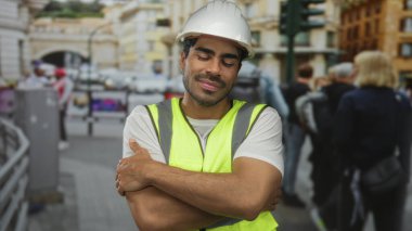 Beyaz yelek ve yelek giyen mühendis gülümsüyor ve kalabalık şehir kalabalığının ortasında duruyor..