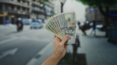 Bir şehir caddesinde dolarları elinde tutan bir adam, Amerikan banknotlarını sergiliyor, açık havada şehir ortamında.