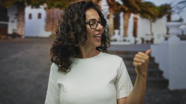 Beyaz tişörtlü orta yaşlı kadın eski şehir caddesini işaret ediyor..