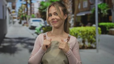 Sarışın, elleri sımsıkı bağlanmış ve sokakta tatlı tatlı gülümseyen bir kadın; belirsizlik, iç gözlem şüphesi.