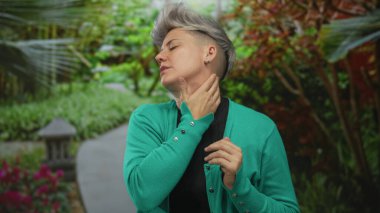 Yeşil hırka giyen kadın boynuna dokunur ve kafasını eğip orman yolunda gözlerini kapatır..