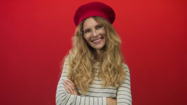 Kollarını kavuşturup stüdyoda gülen bir kadın, kırmızı çizgili bir duvara karşı bere ve gözlük takan sarışın bir ilham perisi kılığına girmiş..