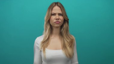 Sarışın kadın, odaklanmış kaşları çatık olarak stüdyoda doğrudan kamerayı işaret ediyor..