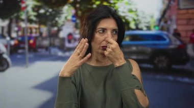 İspanyol kadın, şehir merkezindeki işlek caddede öğleden sonra kaldırımın yanındaki arabaların yanında burun sıkıyor..