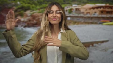 Kadın gülümseyen bir ifadeyle kollarını kaldırıyor kumlu sahilde açık jestler sergiliyor; iyimserlik sıcak karşılanıyor.