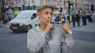Çizgili gömlekli kadın şehirde parmak ucuyla sağa sola, parmak dudakla sessizlik için ise gizem gösteriyor..