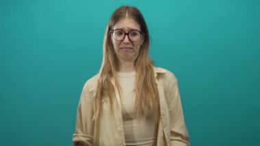 Krem rengi gömlek giyen, burnu kırışık, parlak ışıklar altında alnı çatık bir kadın..