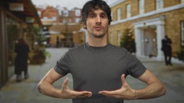 Gri gömlekli genç adam öne doğru eğiliyor ve iki elini de şehir caddesinde göğsünden tutuyor..