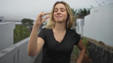 Sarışın genç kadın, beyaz duvarlı dar bir sokakta küçük bir boşluk göstermek için parmaklarını çimdikliyor..