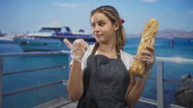 Kadın fırıncı baget tutuyor ve eldiven parmağıyla deniz kenarındaki iskelede, sahil pastanesinde huzur içinde..