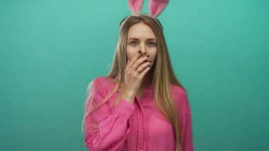 Pembe tişörtlü, tavşan kulaklı genç kadın yeşil arka plan duvarına karşı duruyor..