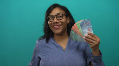 Stüdyoda deniz mavisi arkaplanlı, halkalı banknotları sayan kadın, zenginlik refah başarı bolluğu.