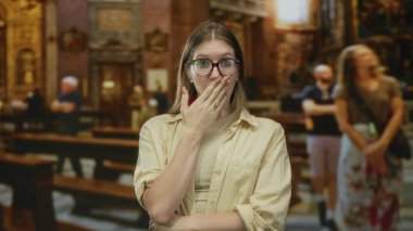 Süslü kilise binasında dururken, gözlüklü sarışın kadın ağzını eliyle kapatıyor. Sürpriz..