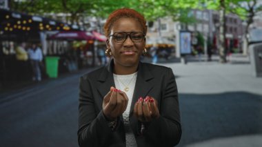 Siyah ceketli ve beyaz gömlekli bir kadın para içinde avuç içi kaldırıyor. Meşgul şehir caddesinde jest yapıyor. Çaresizlik..