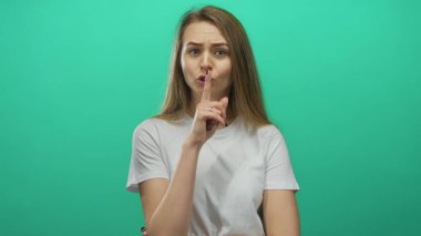 Yeşil arka planda sessizce susan bir kadın, düşünceli bir ifadeyle günlük beyaz bir gömlek içinde sessizliğini koruyor.