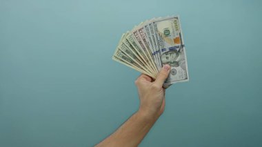 Beyaz adam, Amerika Birleşik Devletleri 'nin dolar banknotlarından oluşan bir hayranıyla sağlam bir mavi duvar arkasında para ve finansal başarı sergiliyor..