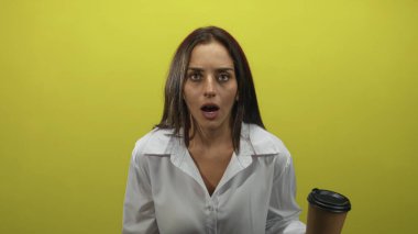 Sarı stüdyoda, tek kullanımlık kahve bardağını elinde tutan ve kaşlarını kaldıran genç İspanyol kadın. Sürpriz yorgunluk..