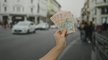 Romen lei banknotlarını elinde tutan adam şehir sokaklarında, şehir içi halk ve binalara karşı para gösteriyor..