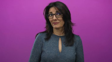 Orta yaşlı, gözlüklü İspanyol kadın ağzını açar ve stüdyoda mor arka planla gözlerini açar..