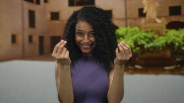 Genç İspanyol kadın, eski bir kasaba sokaklarına para harcamak için sakince parmak uçlarını ovalıyor; tüketim alışverişi alışveriş harcamaları perakende satış finansmanı ekonomi ödeme bütçesi.