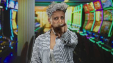 Renkli neon ışıkların altında slot makinesini işaret eden kadın gözleri kapalıyken; şüphe.