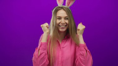 Pembe gömlekli, paskalya tavşanı kulaklı genç bir kadın mor arka planda şakacı yüzünü örtüyor..