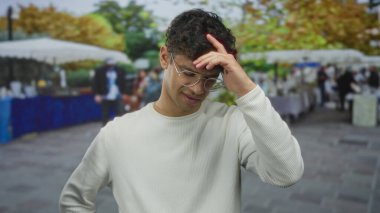 Gözlüklü ve beyaz tişörtlü bir adam, şehirdeki sokak pazarında el ele kıvırcık saçlara dokunuyor..