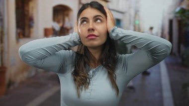 Canlı sokak gösterilerinde kulaklarını tutan bir kadın gürültülü şehirliler arasında stres yaratıyor, açık havada mavi gömlek giyiyor ve canlı şehir manzarası yaratıyor..