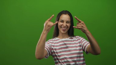 Yeşil bir stüdyoda, üzerinde çizgili tişört ve hatta ışıklandırmalı şakacı bir eğlence seti olan iki eliyle boynuzlarını gösteren bir kadın..