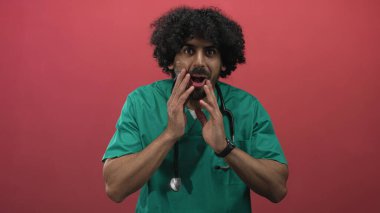 Stüdyoda steteskoplu yeşil önlüklü adam doktor. Kırmızı arka planlı elden ağıza. Sürpriz acil sağlık tavsiyesi..