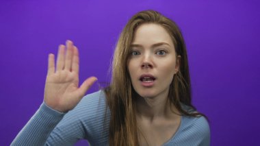 Mavi kazaklı genç beyaz kadın elini kaldırıyor ve stüdyoda ağzı açık bir şekilde parmağıyla işaret ediyor..