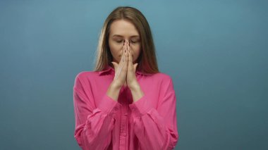 Canlı pembe tişörtlü, izole edilmiş mavi arka planda meditasyon yapan bir kadın sükunet ve farkındalık sergiliyor..