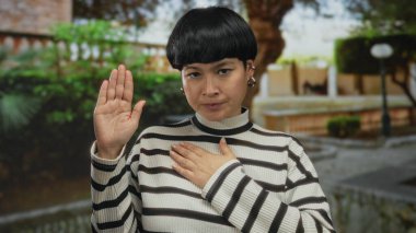 Parkta bağlılık yemini eden bir kadın çizgili bir kazak giyiyor, yeşilliklerle çevrili, içtenlik ve açık hava sükuneti duygusu taşıyor..