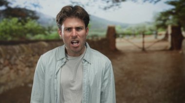 Ağzı açık bağıran bir adam, yüzü görünen bir adam ve bir kırsal sokakta bir kapı yakınında çıplak dişler; öfke yüzleşmesi.