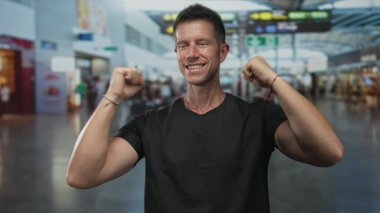 Yumruklarını sıkan ve kollarını kaldıran, gülümseyen ve yoğun havaalanı terminalinde siyah tişört giyen adam; keyif yolculuğu başarısı.