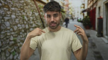 Taş duvar ve bulanık yayalar ile dar bir sokakta göğsü gösteren genç adam parmağı; belirsizlik şüphesi kafa karışıklığı.