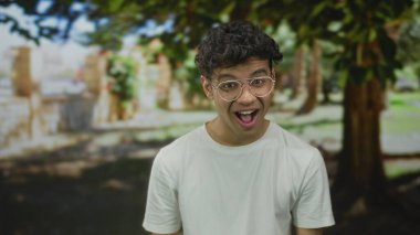 Ormanda ağzı açık ve gözlüklü bir adam, benekli güneş ışığı altında beyaz gömlek giyerek esniyor; yorgunluk.