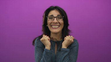 Gözlüklü kadın yüzünü mor stüdyo ortamında iki eliyle örtüyor. Gözlük ve yüzüklerle vurgulanan ifade..