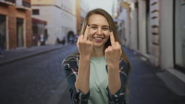 Şehrin arka planında ifade vermek için orta parmakları mizahi bir şekilde kaldırılmış, günlük ekose gömlekli bir kadın..