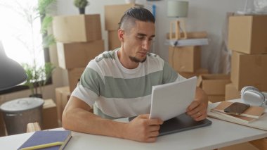 Taşınan kutular ve defterlerle çevrili, evrak okuyan ve telefonu kontrol eden bir adam, planlama tefekkürünün ayarlanması,.