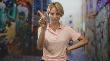 İşaret parmağı önde, el kalçada, pembe polo gömlek ve görünür önkol giyen bir kadın, uyarı otoritesi.