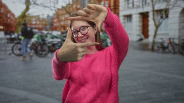Şehir sokaklarında pembe kazak giyen genç sarışın kadın parmakları ile yüz yüze; oyuncu yaratıcılık.