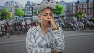 Şehir caddesinde bisiklet kiralama parkına karşı çenesinde dinlenen kısa gri saçlı kadın; tefekkür.