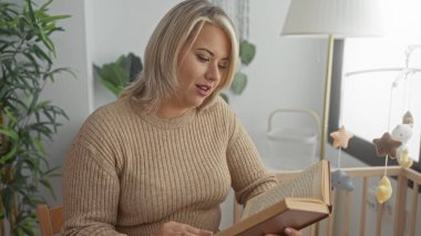 Sarışın kadın yatak odasındaki sıcak lambanın altında hareketli beşiği olan masal kitabı okuyor. Huzur..